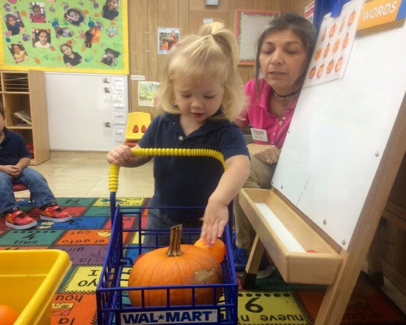 Teacher guiding a child during a pumpkin learning activity at Horizons Childcare & Learning Center.